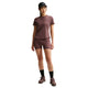 En person er iført en matchende lilla Nike Swift SS løbetop (Dame, Tattoo/Reflective Silv) og shorts, stylet med en sort kasket, strømper og lilla sneakers. Dri-FIT-materialet og de diskrete Nike-logoer fremhæver det sporty look mod en hvid baggrund.