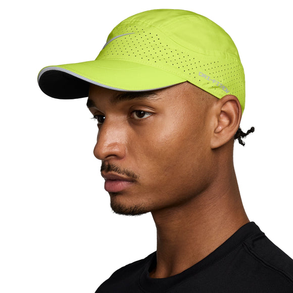 En person i profil bærer en Nike Unstructured Reflective Cap (Unisex, Cyber/Anthracite/Reflective Silv) med fugttransporterende teknologi og en sort sportstrøje, poseret mod en ensfarvet baggrund.