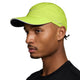 En person i profil bærer en Nike Unstructured Reflective Cap (Unisex, Cyber/Anthracite/Reflective Silv) med fugttransporterende teknologi og en sort sportstrøje, poseret mod en ensfarvet baggrund.