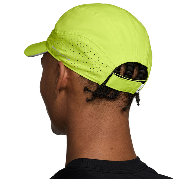 En person med korte snoninger bærer en Nike Unstructured Reflective Cap i Cyber/Anthracite/Reflective Silver med perforeret design og justerbar rem bagpå, set bagfra.