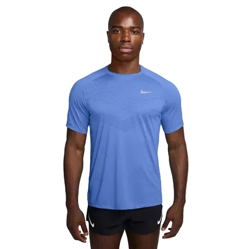 En person ser frem for sig iført en kongeblå Nike Stride SS Running Top, Herre, Royal Pulse/Reflective Silv med en lille hvid swoosh på brystet og sorte shorts. Baggrunden er helt hvid.