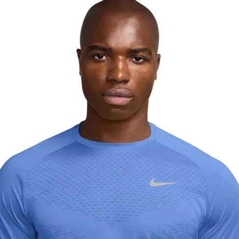 En person med barberet hoved bærer en lyseblå Nike Stride SS Løbetop, Herre, Royal Pulse/Reflective Silv, og ser lige frem med et neutralt udtryk. Denne tekniske løbetrøje er designet til optimal komfort og ydeevne.