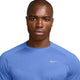En person med barberet hoved bærer en lyseblå Nike Stride SS Løbetop, Herre, Royal Pulse/Reflective Silv, og ser lige frem med et neutralt udtryk. Denne tekniske løbetrøje er designet til optimal komfort og ydeevne.
