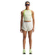 En kvinde kigger fremad iført en lysegrøn ærmeløs top, Nike AeroSwift 3In løbeshorts til kvinder i off white/hvid/sort, grønne løbesko og store reflekterende solbriller mod en hvid baggrund.