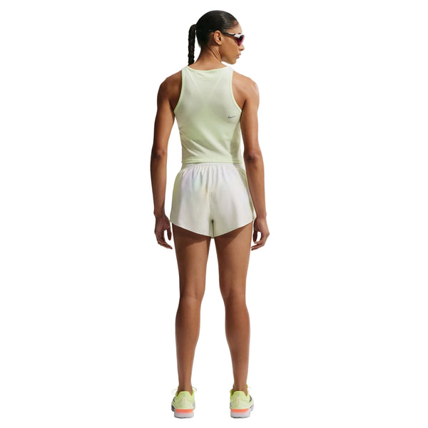 En kvinde med fletning, iført solbriller, en ærmeløs lysegrøn sportstop, Nike AeroSwift 3In løbeshorts til kvinder i Off White/White/Black og lysegrønne løbesko står med ansigtet vendt mod kameraet på en almindelig hvid baggrund.