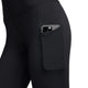 Et nærbillede af en person, der har Nike One High-Waisted 7/8, Dame, Black/Black-træningstights på, med en smartphone i sidelommen. Nike-træningstightsene er udstyret med Dri-FIT-teknologi og er fotograferet foran en ensfarvet hvid baggrund.