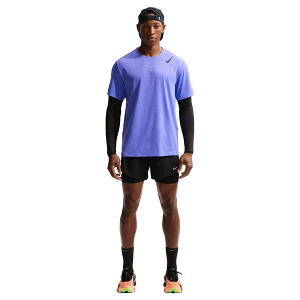En mand ser frem for sig iført en safirfarvet/sort Nike Nk Dfadv Aroswft SS Top, sorte shorts, sorte ærmer og sokker, neonfarvede løbesko og en bagudvendt sort kasket på en almindelig hvid baggrund.