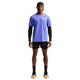 En mand ser frem for sig iført en safirfarvet/sort Nike Nk Dfadv Aroswft SS Top, sorte shorts, sorte ærmer og sokker, neonfarvede løbesko og en bagudvendt sort kasket på en almindelig hvid baggrund.