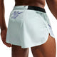 Nærbillede af en person iført Nk Dfadv Arswft Gfx 2Bf Shrt løbeshorts til herrer i Barely Green/Lapis fra Nike, der viser ryg- og sidedetaljer med logoer og perforeret ventilation.