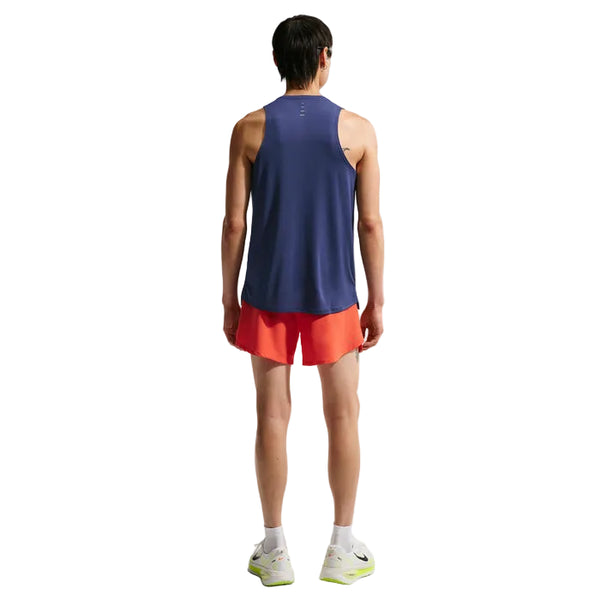 En person kigger væk fra kameraet og er iført en Nike Nk Dfadv Stride Tank til mænd i Midnight Navy/Reflective Silver sammen med røde shorts, hvide sokker og hvide sportssko. Baggrunden er helt hvid.