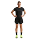 En person står med ansigtet fremad og hænderne på hofterne, iført en sort Nike t-shirt, Nike Nk One Df Hr 3In 2N1 Short, Dame, Black/White, sorte sokker og neongule løbesko på en hvid baggrund.