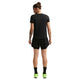En person med knold står med ansigtet væk på en almindelig hvid baggrund, viser tatoveringer på armen og er iført en sort t-shirt, Nike Nk One Df Hr 3In 2N1 Short Dame i sort/hvid, sorte sokker og neongrønne sneakers.