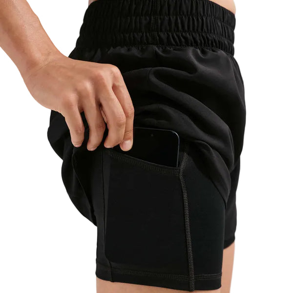 En person løfter det yderste lag af sin Nike Nk One Df Hr 3In 2N1 Short, Dame, Black/White for at afsløre en skjult inderlomme med en smartphone.