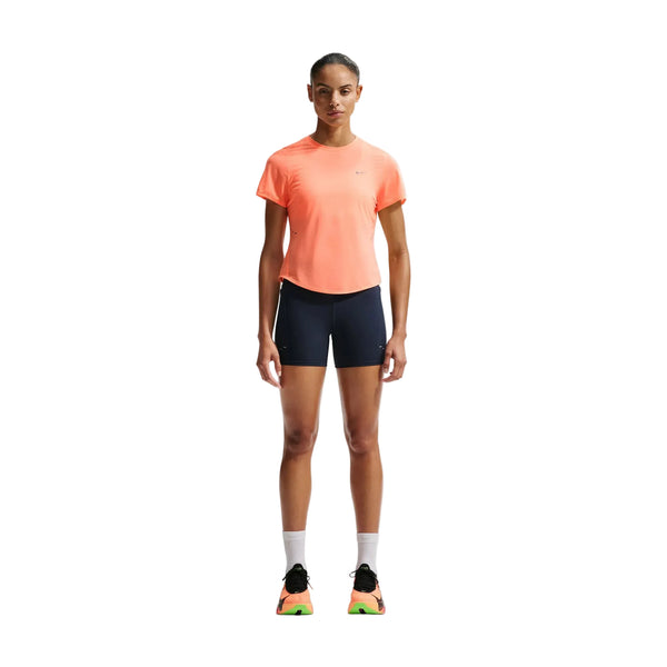 En kvinde kigger fremad iført en koralfarvet Nike Nk Swft Nvlt Brthe Ss Top i Orange Pulse/Photon Dust/Reflective Silver sammen med marineblå shorts, hvide sokker og sorte løbesko - et luftigt outfit, der er perfekt til løbetræning af kvinder på en almindelig hvid baggrund.