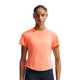 En kvinde ser frem for sig i en lysende orange Nike Nk Swft Nvlt Brthe Ss Top (Dame, Orange Pulse/Photon Dust/Reflective Silv) og mørke leggings, der viser den åndbare løbetræningst-shirt mod kvinder på en almindelig hvid baggrund.
