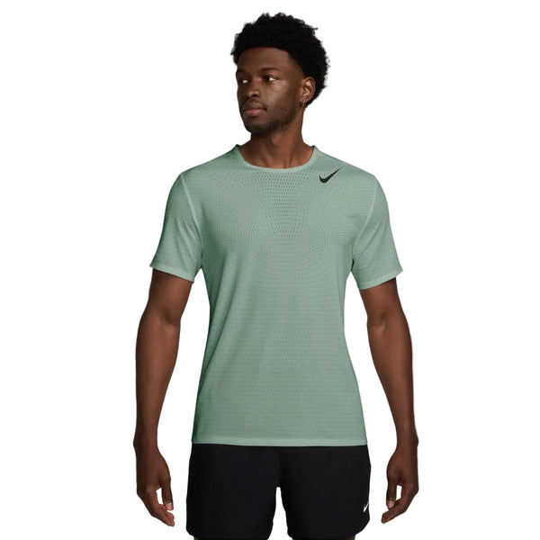 En mand iført en lysegrøn Nike Nk Dfadv Aroswft Ss Top, Herre, Steam/Black og sorte shorts står let vendt mod en almindelig hvid baggrund og fremviser sit ultraløbræning-look.