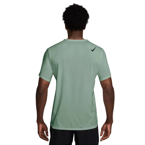 En person ses bagfra iført en Nike Nk Dfadv Aroswft Ss Top, Herre, Steam/Black - en lysegrøn, åndbar mesh-lignende løbetrøje med et sort logo på den øverste højre skulder - sammen med sorte shorts.