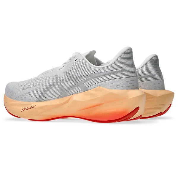 Et par ASICS Novablast 6 Dame-løbesko i farvekombinationen hvid/Vivid Coral med tykke mellemsåler, der er designet til optimal energiretur, og røde ydersåler, vist set skråt bagfra på en hvid baggrund.