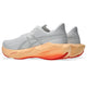 Et par ASICS Novablast 6 Dame-løbesko i farvekombinationen hvid/Vivid Coral med tykke mellemsåler, der er designet til optimal energiretur, og røde ydersåler, vist set skråt bagfra på en hvid baggrund.