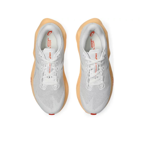 Et par Asics Novablast 6 Dame-sneakers i farvekombinationen hvid/levende koral, med overdel i mesh, der sikrer god åndbarhed, hvide snørebånd, lysebrune såler og logoer i levende koral, ses set ovenfra på en hvid baggrund. Designet til at give optimal energiretur ved hvert skridt.
