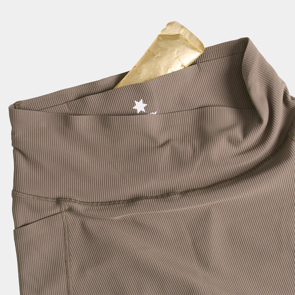 Nærbillede af Saysky W Combat+ Rib Short Tights 4" til kvinder i taupe med ribkant, høj talje med skjult lomme i linningen til en guldfolieindpakket genstand og et lille hvidt korslogo på linningen.