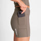 En person iført taupe W Combat+ Rib Short Tights 4" fra Saysky, der har en sidelomme med en sort smartphone delvist indeni. Saysky-mærket er trykt lodret på disse dame træningstights.