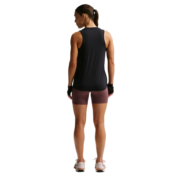 En kvinde kigger væk iført Nike Nk One Classic Df Tank (Dame, Black/White), lilla cykelshorts, hvide sneakers og sorte fingerløse handsker. Hendes hår er sat op i en hestehale mod en hvid baggrund.