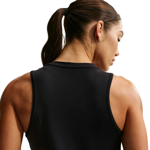 En kvinde med brunt hår i hestehale ses bagfra iført Nike Nk One Classic Df Tank til kvinder i sort/hvid. Hun har hovedet drejet lidt til højre og viser en lille ørering i venstre øre mod en hvid baggrund.