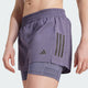 En person er iført Adidas Otr B S 2In1 Dame Previo lilla løbeshorts med sorte striber over matchende kompressionsshorts. Kun underkroppen og overbenene er synlige mod en ensfarvet baggrund.