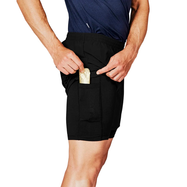 En person iført Saysky Pace 2in1 Running Shorts 5", Herre, Black og en marineblå skjorte lægger en energibar i en sidelomme. Billedet er beskåret, så man kun ser overkroppen og det øverste af benene.