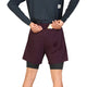 Iført en langærmet trøje og et par Saysky Pace 2-i-1-shorts 5″ til mænd i farven burgundy samt sorte underbukser lægger en person (hvis hoved ikke er synligt) en telefon eller et kort i baglommen på løbeshortsene.