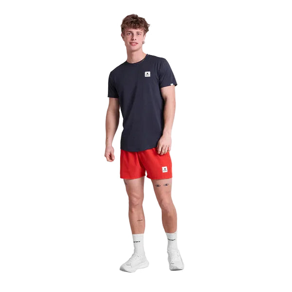 En person står på en hvid baggrund iført en mørk Saysky Herre t-shirt, røde Saysky Pace Shorts 5", hvide strømper og hvide sneakers. Både trøjen og shortsene har små rektangulære Saysky-logoer.