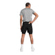 En person står med ryggen til kameraet foran en ensfarvet hvid baggrund. Personen er iført en grå T-shirt, et par Saysky Pace 2-i-1-shorts 5″ til mænd i sort – designet som trail-løbeshorts – hvide sokker og hvide sko, med den ene hånd på hoften og den anden hånd nede i lommen på shortsene.