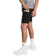 En person iført et par Saysky Pace 2-i-1-shorts 5″ til mænd i sort, med en praktisk mobillomme på låret, samt en grå T-shirt, hvide sokker og hvide sneakers, lægger en lyserød smartphone ned i lommen på shortsene. Kun underkroppen er synlig.