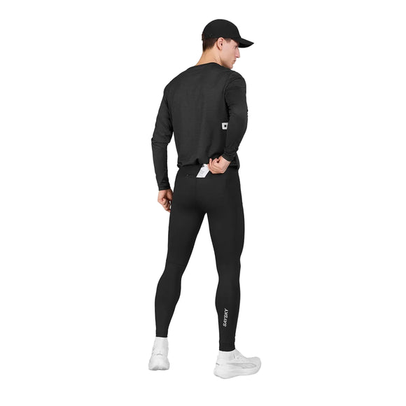 En person iført en sort kasket, en langærmet trøje og Saysky Pace+ lange tights, Herre, Sort står med ryggen til og holder en telefon i baglommen. Outfittet består desuden af hvide sportssko, og de lange tights er forsynet med et lille Saysky-logo.
