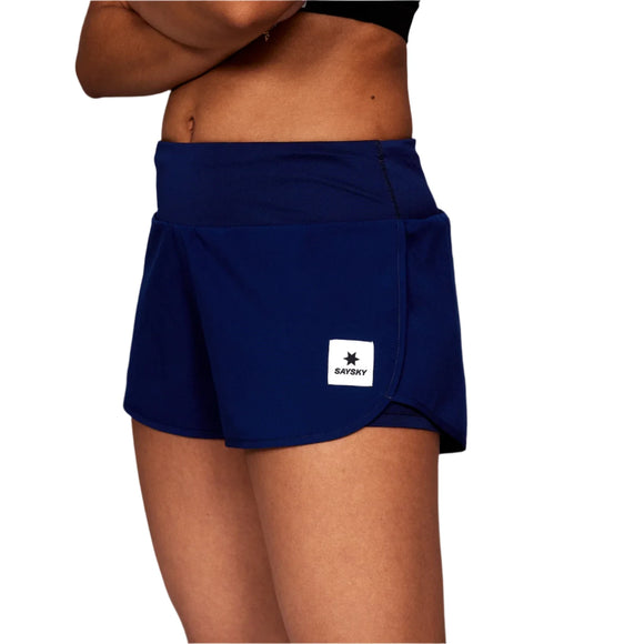En kvinde i sort sports-bh og Saysky W Pace Shorts 3" (Dame, Blue) står med korslagte arme, vist fra midt på torsoen til midt på låret mod en hvid baggrund. Disse shorts blander komfort og stil til aktive kvinder.