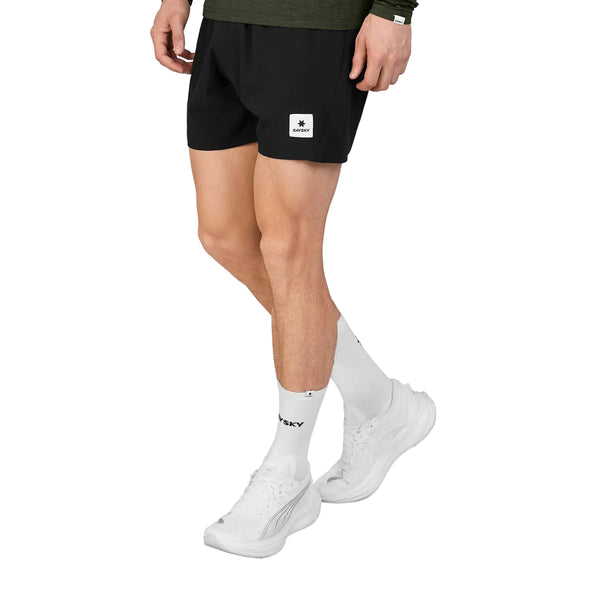 En person iført sorte Saysky Pace Shorts 5″, Herre, Black med et firkantet logo-mærke på låret, hvide sokker og hvide sportssko.