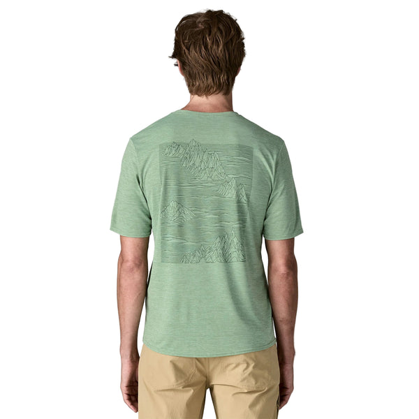 En person med kort brunt hår ses bagfra iført en Patagonia Cap Cool Daily Graphic Shirt, Herre, Strataspire/Ellwood Green X-Dye, med en diskret bjerggrafik og khakifarvede bukser.