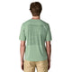 En person med kort brunt hår ses bagfra iført en Patagonia Cap Cool Daily Graphic Shirt, Herre, Strataspire/Ellwood Green X-Dye, med en diskret bjerggrafik og khakifarvede bukser.