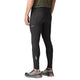 En person står med ryggen til og har Patagonia Peak Mission Tights, Herre, sort, på, kombineret med en grøn trøje og grå løbesko med røde såler. Tightsene har et lille Patagonia-logo og en reflekterende detalje på underbenet. Baggrunden er ensfarvet hvid.