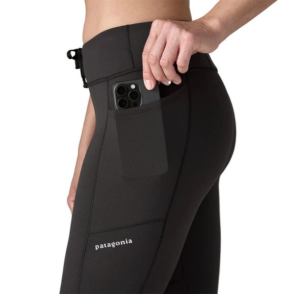 En person lægger en smartphone i sidelommen på de sorte Patagonia Peak Mission Tights 27", Dame. Billedet, der er beskåret til talje og lår, fremhæver telefonen og lommen - perfekte træningstights til løbetights dame-behov.