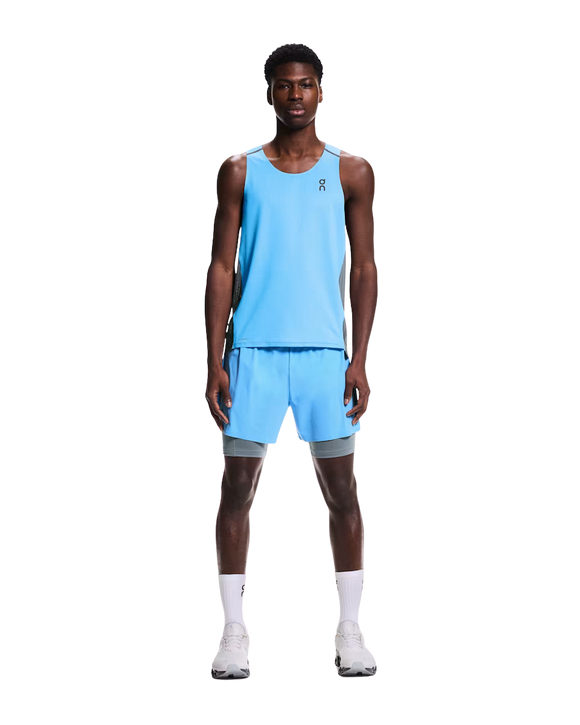 En mand kigger fremad iført On Performance Tank, Herre i Gourami/Rock med matchende shorts, hvide sokker og hvide løbesko på en almindelig hvid baggrund.