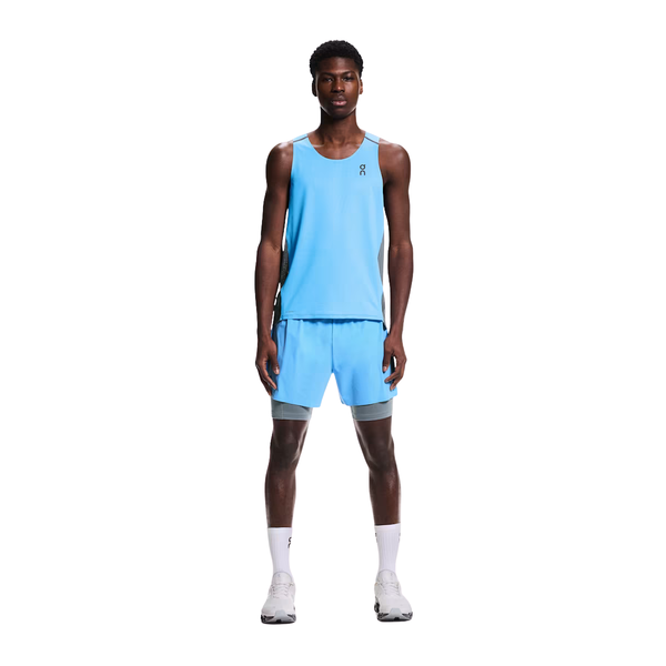 En mand kigger fremad iført On Performance Tank, Herre i Gourami/Rock med matchende shorts, hvide sokker og hvide løbesko på en almindelig hvid baggrund.