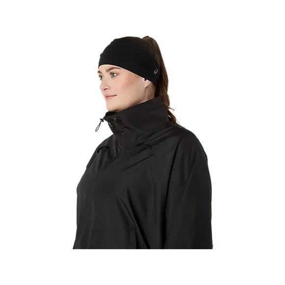 En person iført en sort jakke med høj krave og et Asics Performance-pandebånd (unisex) i farven Performance Black ses i profil på en ensfarvet hvid baggrund. Personen, der er klar til løb eller andre sportslige aktiviteter, har lys hud og brunt hår, der er sat op.