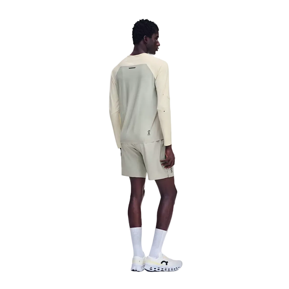 En mand står med ryggen til og har en On Performance Long-T til mænd i farvekombinationen Hare/Brume på samt matchende shorts i åndbart materiale, hvidt par sokker og hvide sportssko. Baggrunden er ensfarvet hvid.