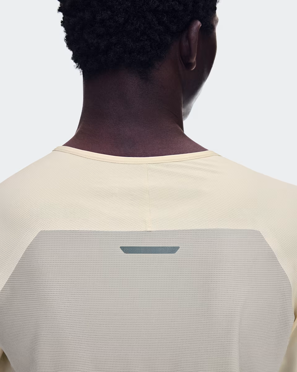 Der ses et billede bagfra af en person med kort, krøllet hår, der bærer On Performance Long-T, Herre, Hare/Brume. Den lysbeige langærmede løbetrøje er fremstillet af åndbart materiale og har en lille reflekterende detalje øverst på ryggen. Baggrunden er ensfarvet og lys.