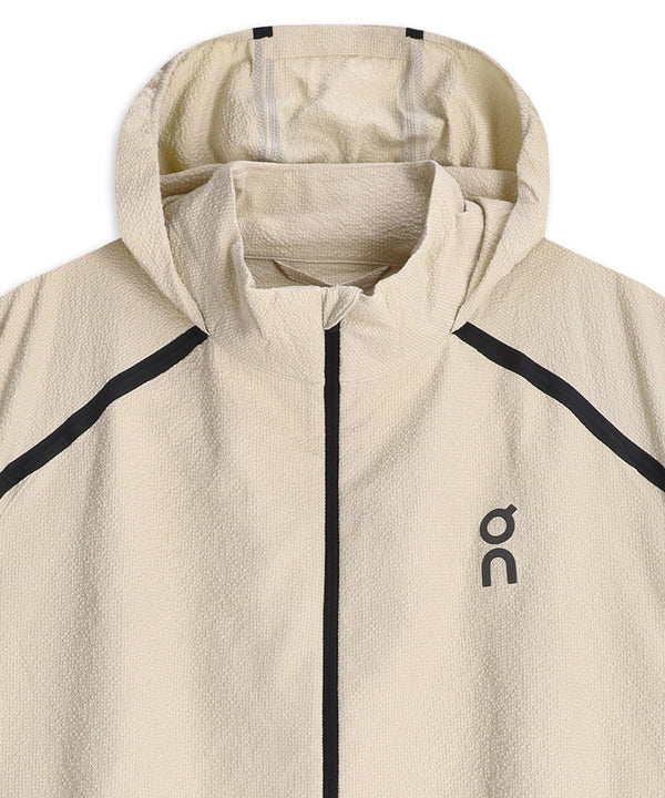 Beige ON Performance Volt-jakke, herre, i farven Hare med sort lynlås og sorte diagonale kontrastlinjer på skuldrene. ON-logoet er trykt på venstre bryst. Denne ultralette løbejakke har et struktureret stof, høj krave og en sammenpakkelig hætte for ekstra komfort.