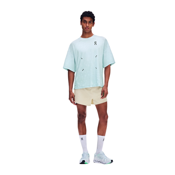 En mand står med ansigtet vendt fremad iført en lyseblå, oversized T-shirt, ON Performance Volt Shorts, Herre, Hare i beige, hvide strømper og hvide sportssko. Den ensfarvede hvide baggrund fremhæver de vind- og vandafvisende løbeshorts, der sikrer komfort i al slags vejr.