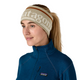 Personen bærer et Patagonia Powder Town-pandebånd (unisex, Hut Tripper-logo: Weathered Stone) fremstillet af genanvendt polyester samt en blå Patagonia-fleecejakke, og har håret sat op i en hestehale. Den hvide baggrund antyder, at personen gør sig klar til vinterløb.