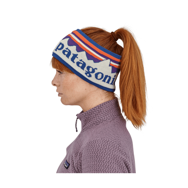 En person med rødt hår i hestehale bærer et Patagonia Powder Town-pandebånd (unisex) i farvekombinationen »Hut Tripper Stripe: Birch White« sammen med en struktureret lavendelblå Patagonia-trøje. Profilbilledet vises på en hvid baggrund.
